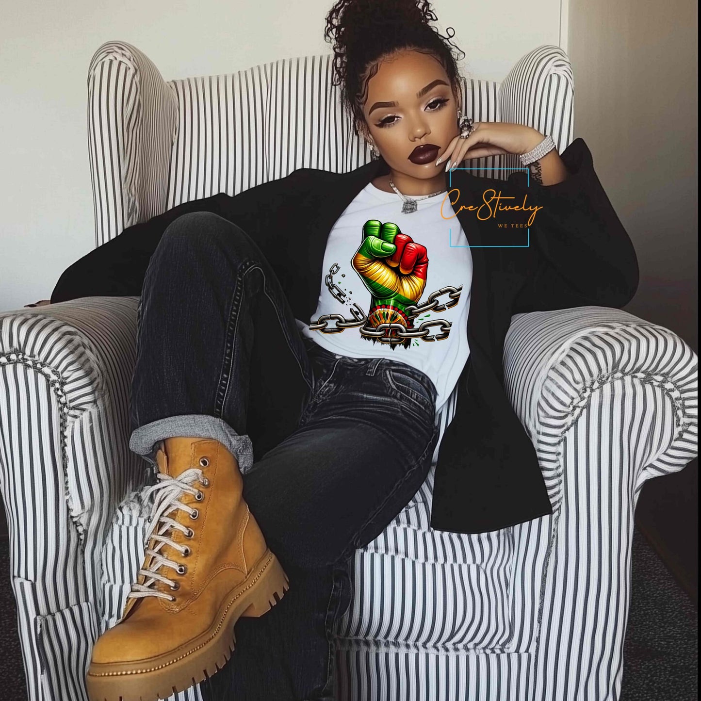 Stylish woman lounging in a chair wearing a bold t-shirt with a raised RBG (Red, Black, Green) fist breaking free from chains, symbolizing Black liberation and power.