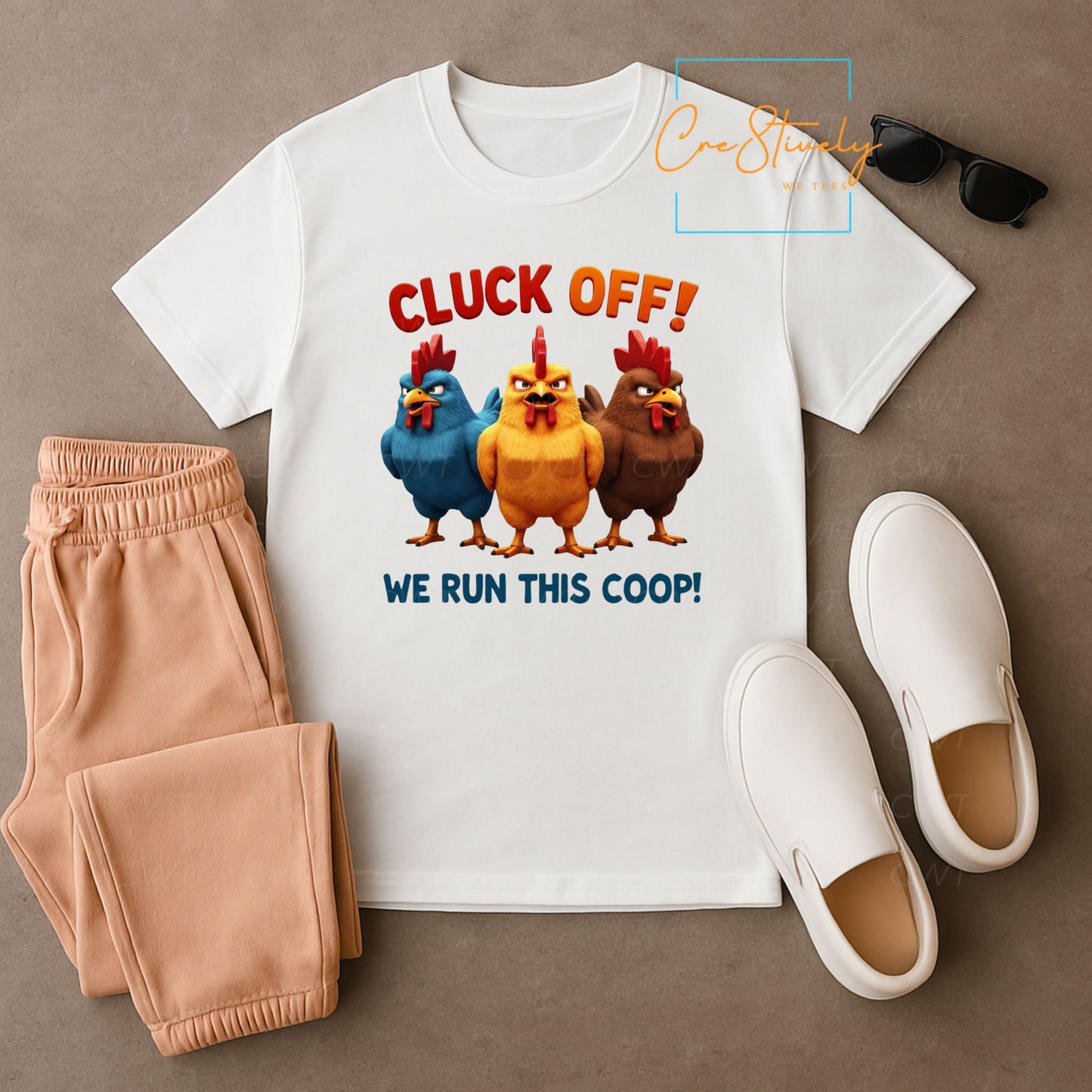 Flat lay of a white t-shirt with three animated hens in blue, yellow, and brown under the phrase “Cluck Off! We Run This Coop!” styled with peach pants, white slip-ons, and sunglasses.