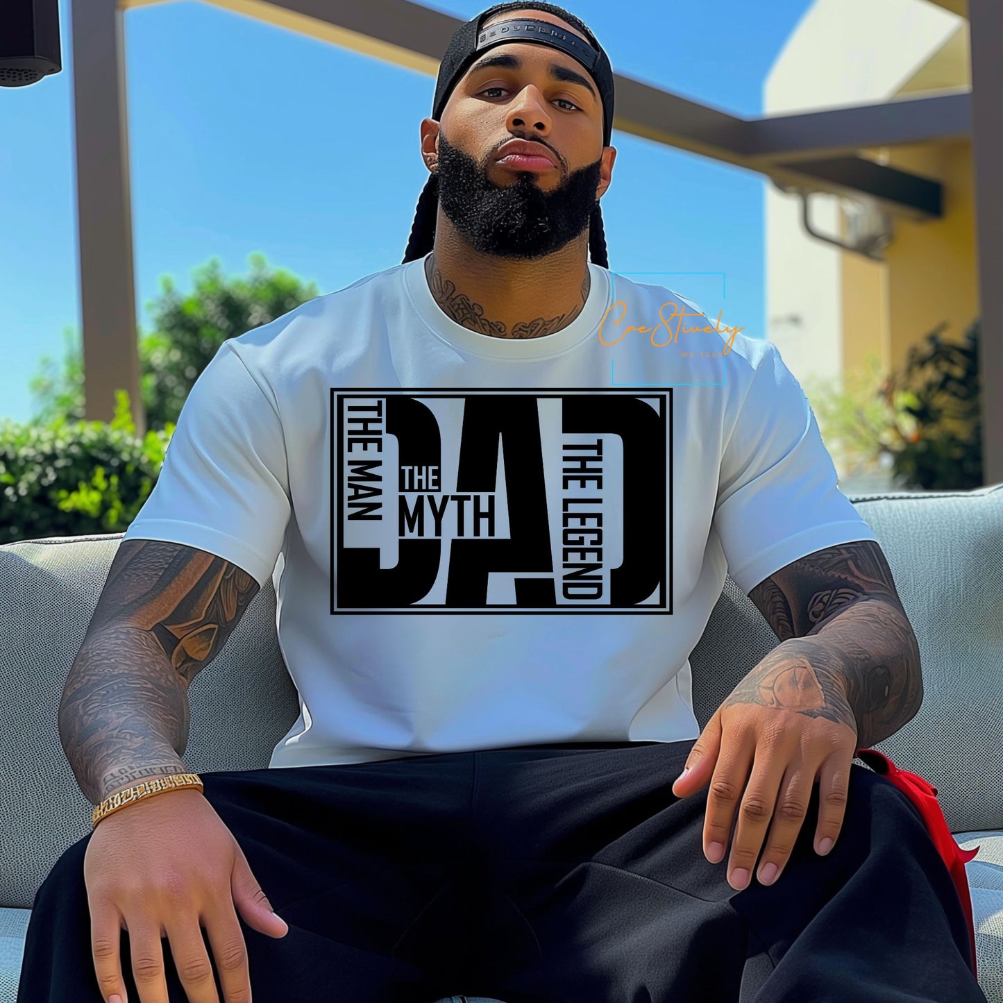 Man sitting confidently wearing a white t-shirt with bold black text that reads “The Man. The Myth. The Dad. The Legend.”
