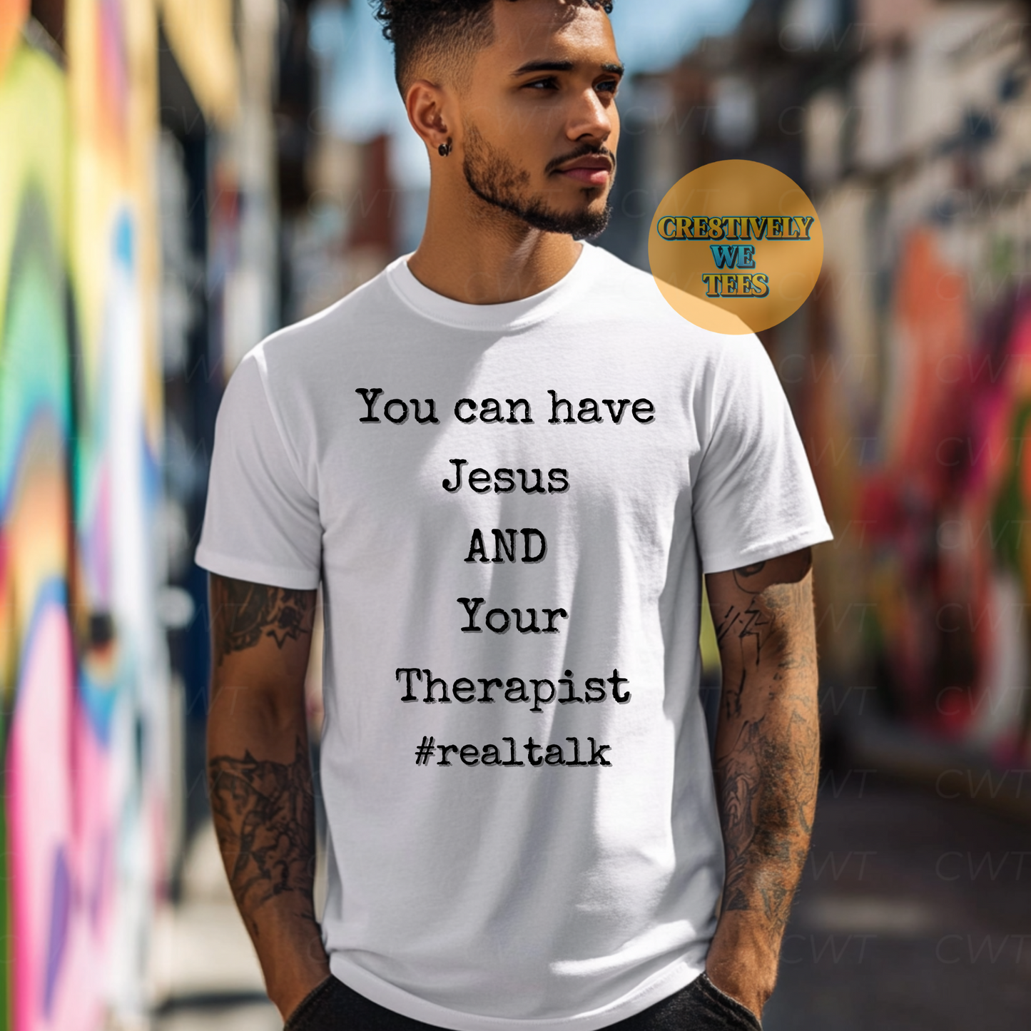 Young man in a white T-shirt featuring the phrase “You can have Jesus AND your therapist #realtalk,” posing casually near a colorful urban background.