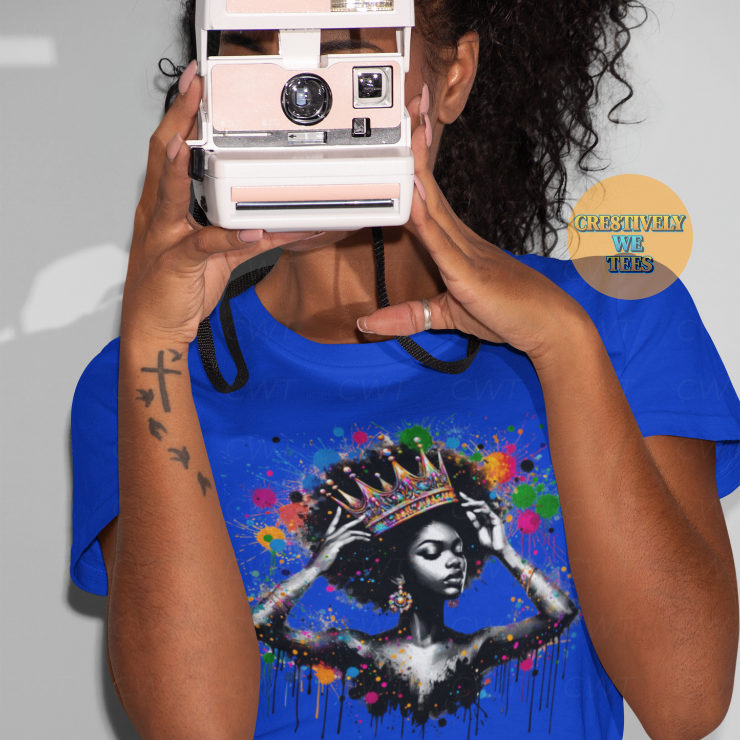 Blue Queen Things t-shirt featuring vibrant Black woman with crown and paint splashes, modeled by woman with vintage camera.