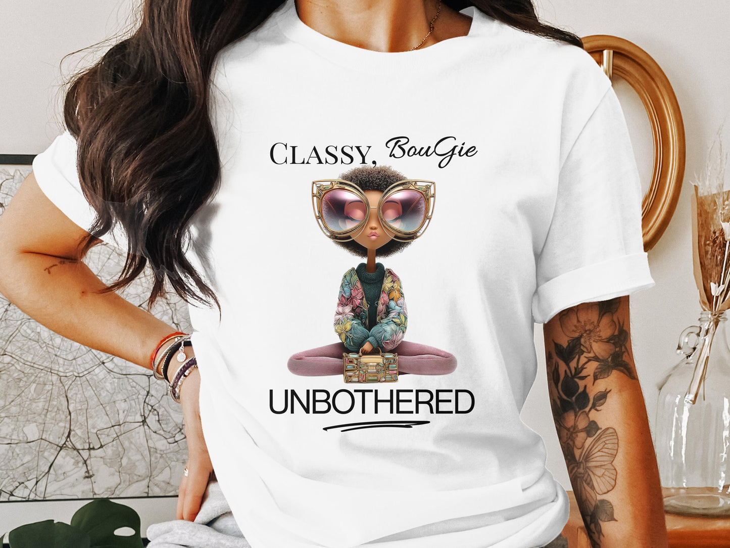 Black woman wearing a white t-shirt that reads “Classy, Bougie, Unbothered” with a bold character design, accessorized with stacked bracelets, posed against a modern background.