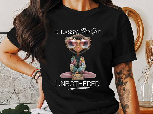 Black woman wearing a black t-shirt that reads “Classy, Bougie, Unbothered” with an illustrated character in sunglasses and floral sleeves, styled casually indoors.