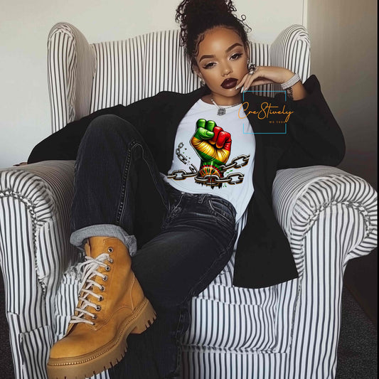 Stylish woman lounging in a chair wearing a bold t-shirt with a raised RBG (Red, Black, Green) fist breaking free from chains, symbolizing Black liberation and power.