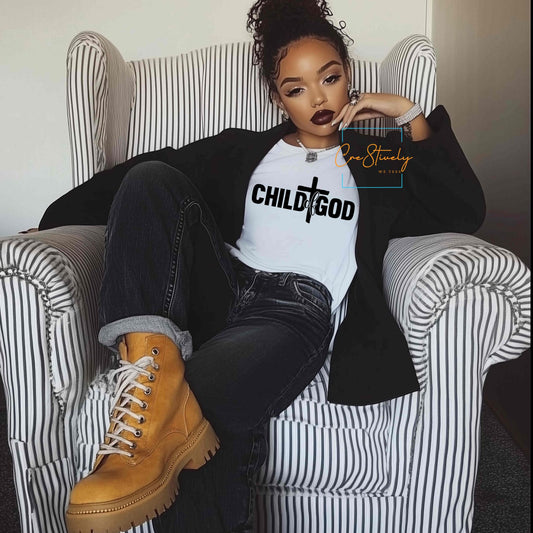 A woman sitting confidently in a striped armchair wearing a white t-shirt with bold black text that reads “Child of God” with a cross between the words. Stylish Christian fashion for modern believers.