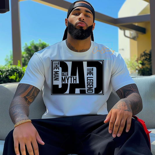 Man sitting confidently wearing a white t-shirt with bold black text that reads “The Man. The Myth. The Dad. The Legend.”