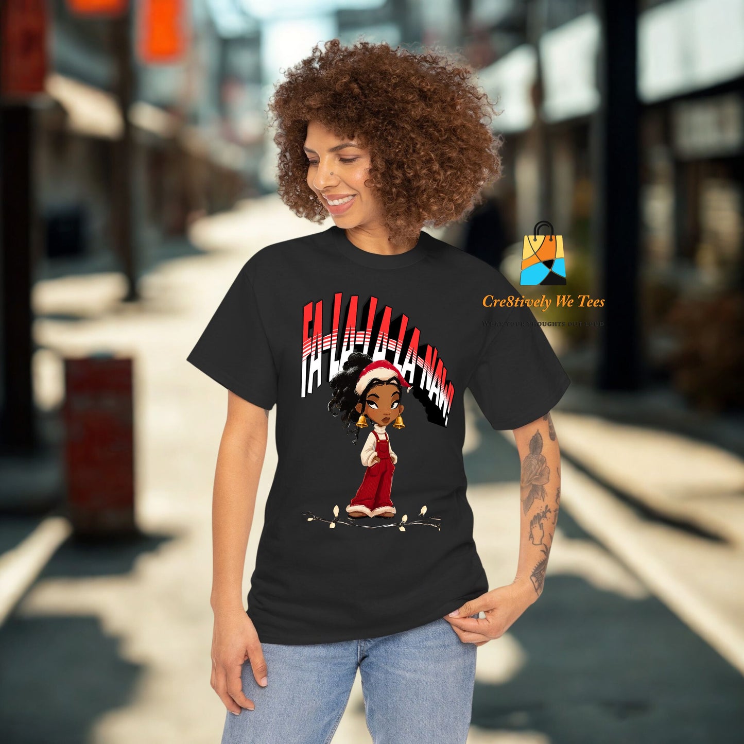 A smiling Black woman wearing a black t-shirt that features the phrase “Falala-la-Naw” with a confident cartoon Black girl in red overalls and Santa hat. Perfect for sassy holiday vibes.