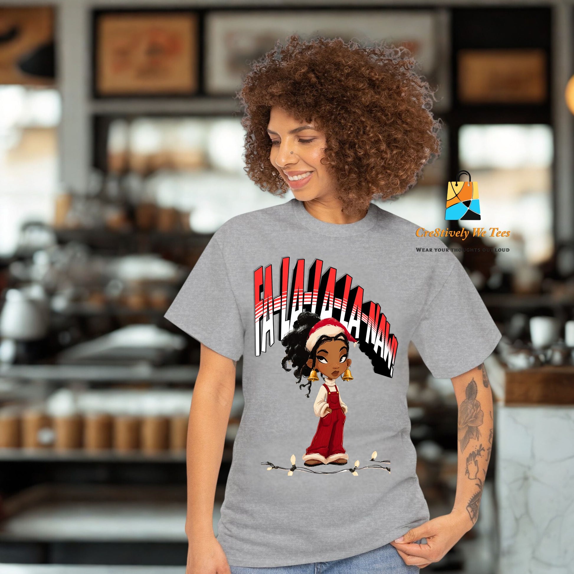 A cheerful Black woman modeling a heather grey unisex t-shirt with a festive “Falala-la-Naw” design. The design includes a stylish Black cartoon girl standing in front of bold holiday lettering.