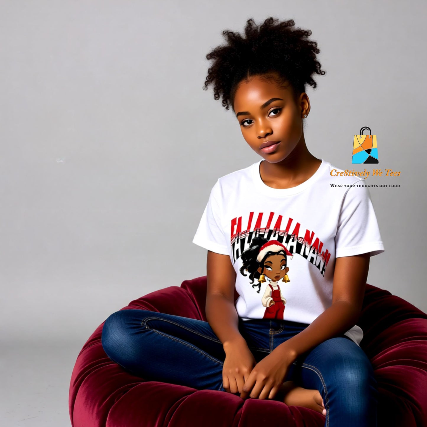 A young Black girl with a soft natural puff sits on a velvet chair wearing a white Falala-la-Naw t-shirt.