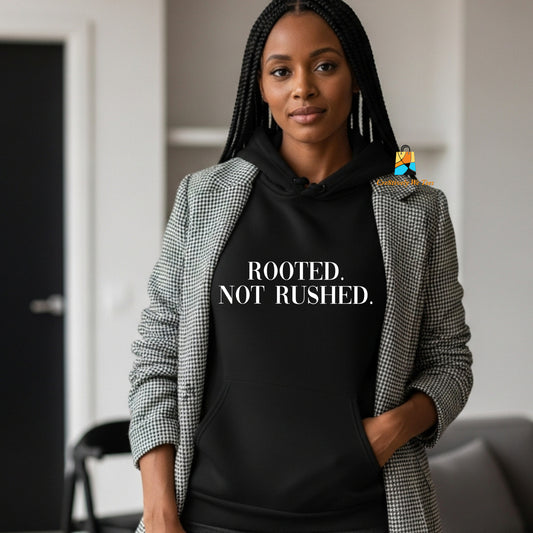 Person wearing a black hoodie with 'ROOTED. NOT RUSHED.' text, standing indoors.