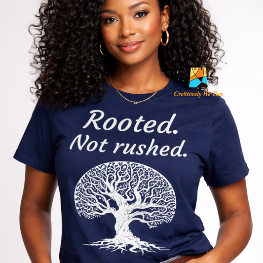 Woman wearing a navy blue t-shirt with a tree design and text 'Rooted. Not rushed.' on a white background.