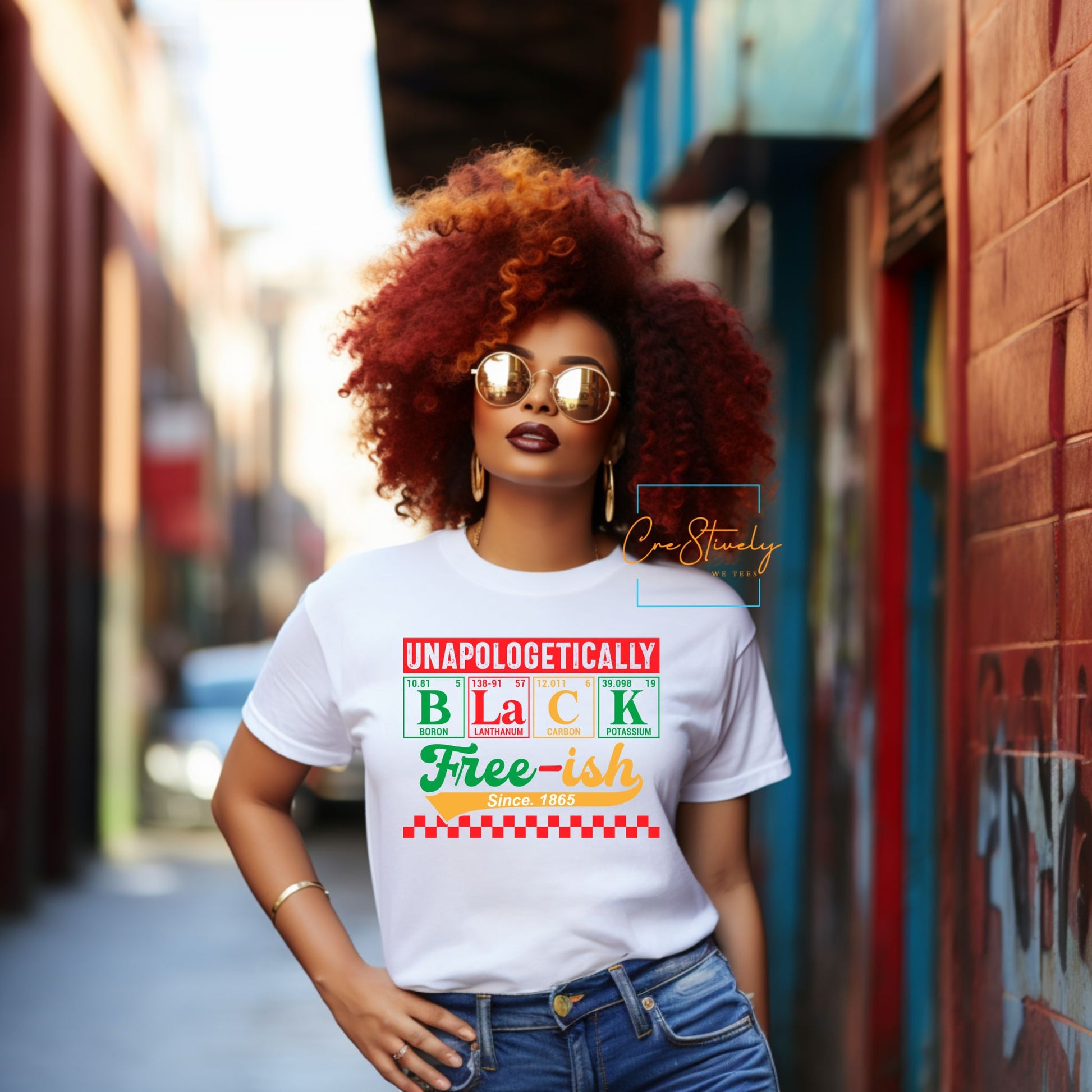 Confident woman with natural red curls wearing a white “Unapologetically Black, Free-ish Since 1865” t-shirt designed with periodic table elements and vibrant Pan-African colors.