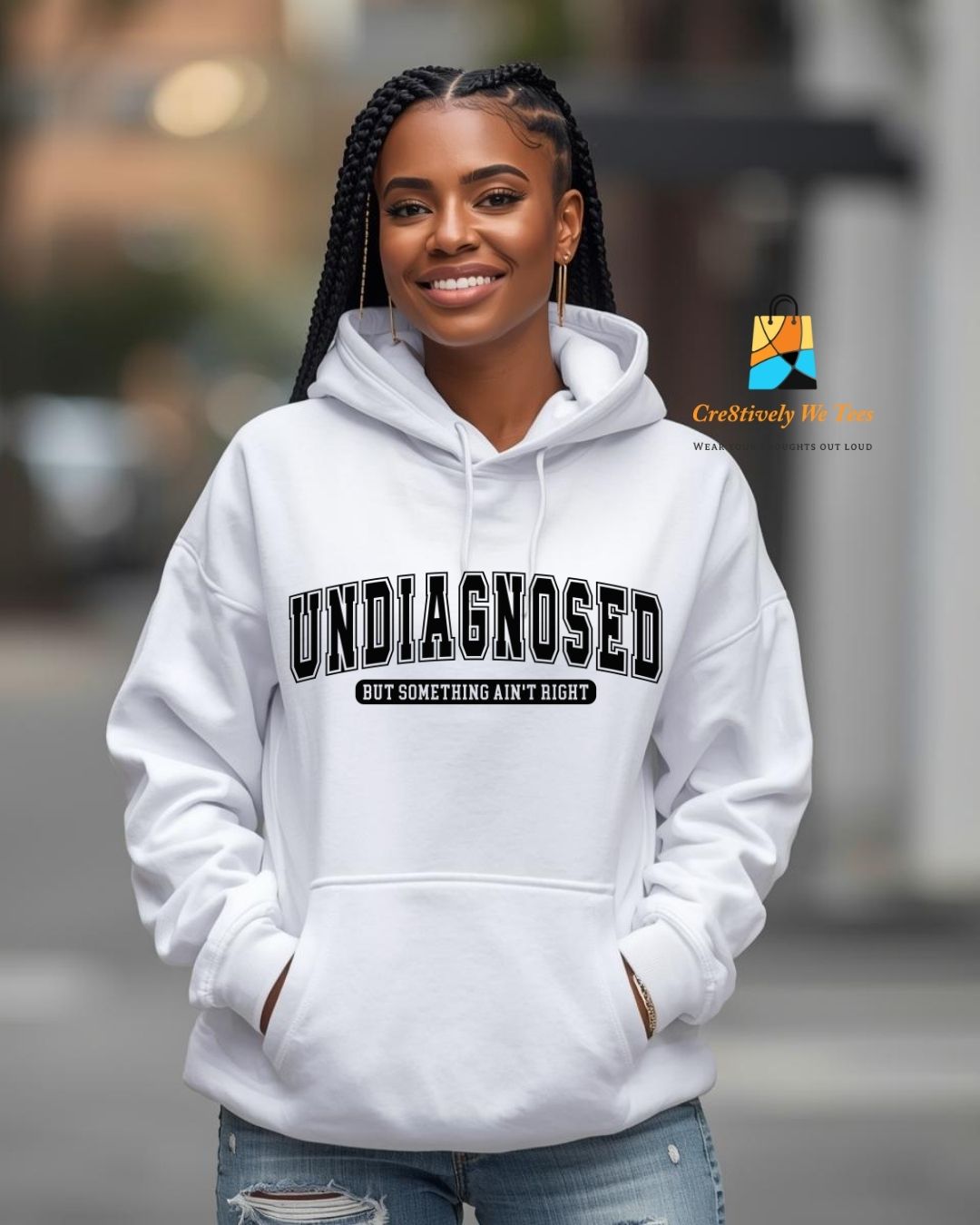 Person wearing a white hoodie with text that says 'Undiagnosed, but something ain't righ' in varsity style lettering, standing outdoors.